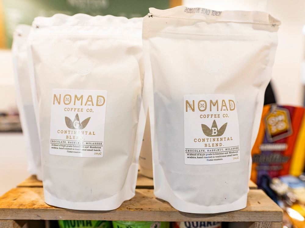 Two 250g bags of Nomad Continental Blend on a wooden crate, one whole bean and one ground