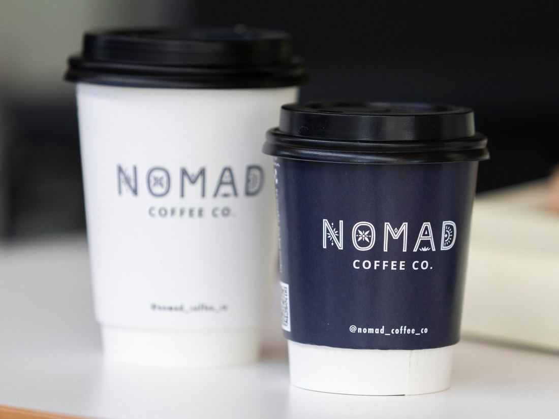 A white and a navy Nomad Coffee Co. takeaway cup side by side