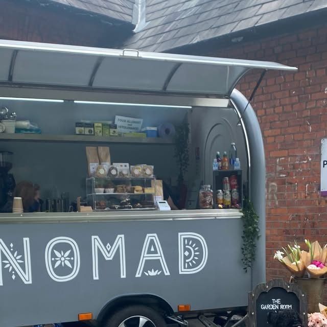 The grey Nomad coffee van with its awning up outside a brick building