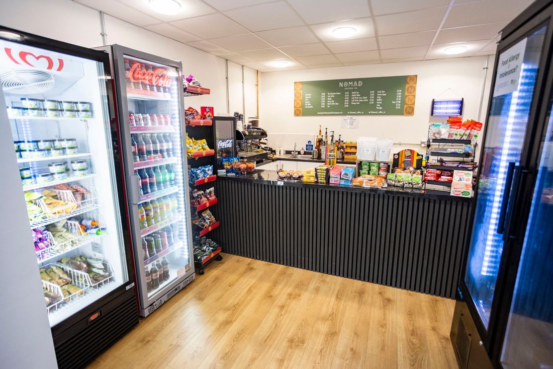 Inside the Parkway café: fridges of cold drinks, a counter of bakes and snacks, and the green menu board