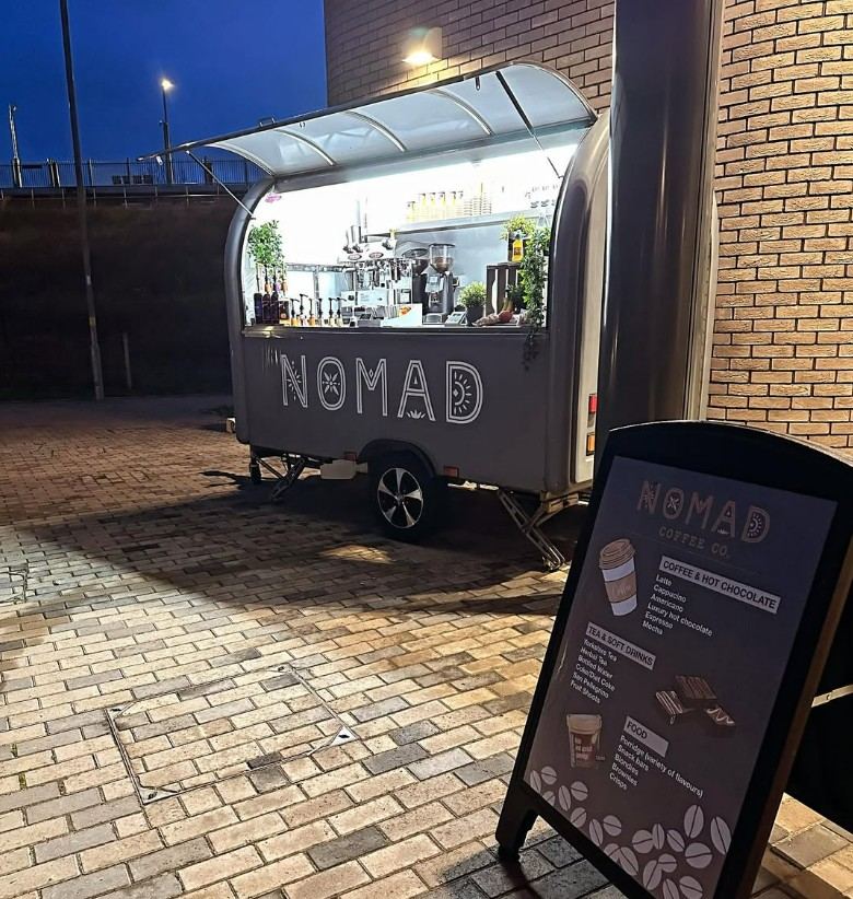 The Nomad coffee van lit up at dusk with its A-board menu